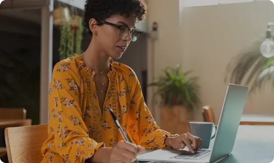 Mulher mexendo no notebook e fazendo anotacoes
